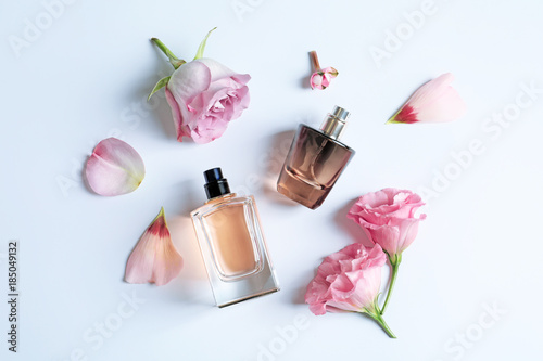 Bottles of perfume with flowers on light background