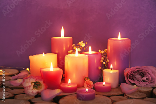 Purple burning candles with flowers on color background