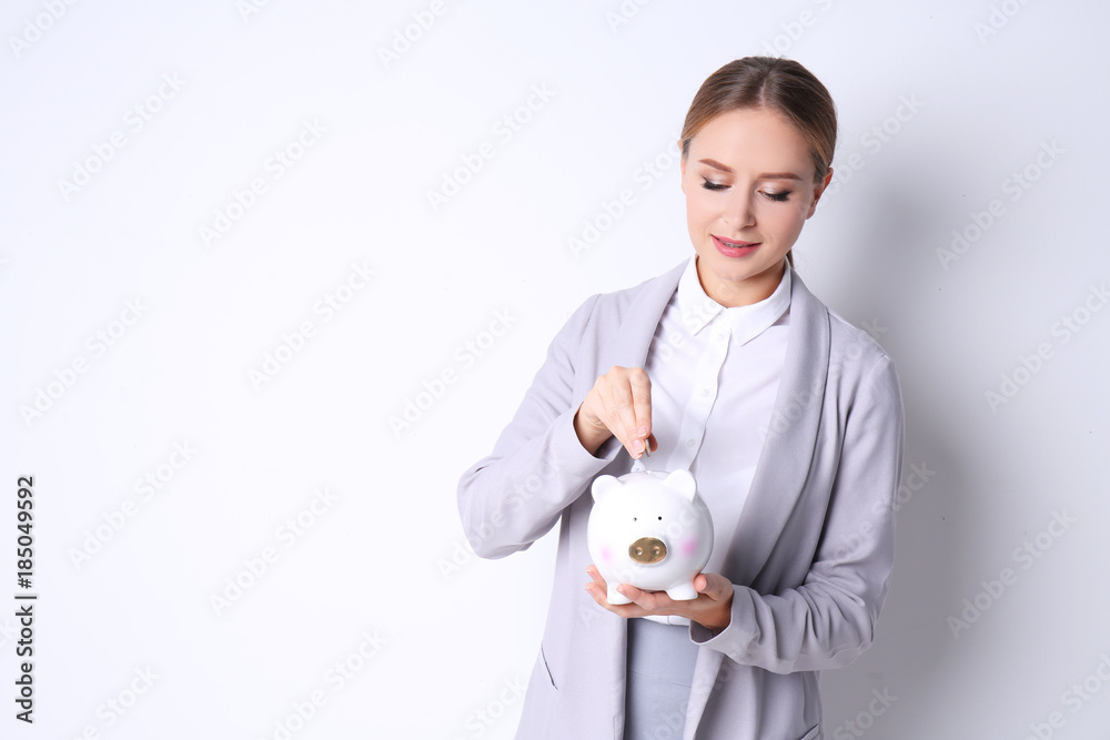 Young woman in formal clothes putting coin into piggy bank on white background Young woman in formal clothes putting coin into piggy bank on white background