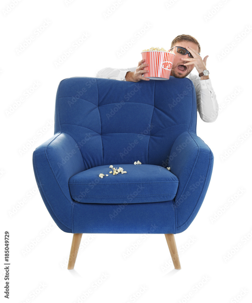 Naklejka premium Scared man with 3d glasses and popcorn hiding behind armchair during cinema show on white background