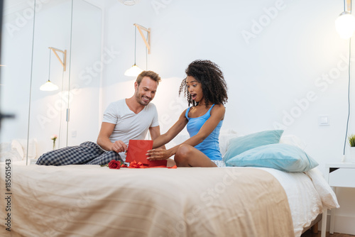 Young beautiful interracial couple in bed giving a surprise gift and rose .