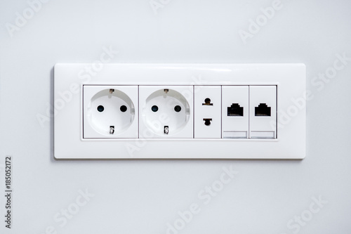 a socket on a light gray wall, a multifunction outlet with an internet connection, two European-style outlets and one American type outlet.