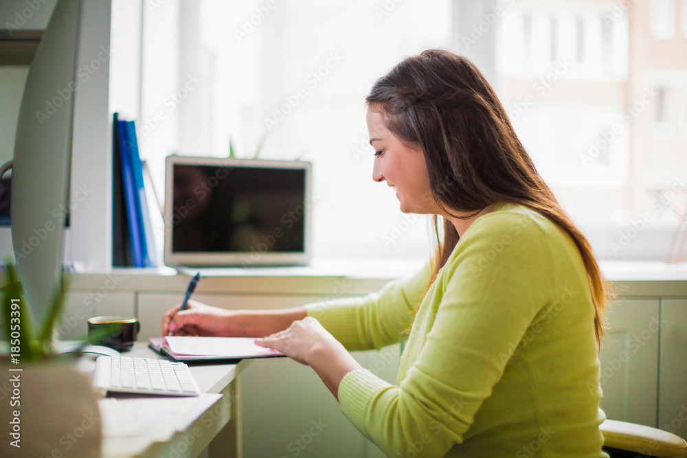 Side view of the young smiling business lady who sitting in the office and writing in a notebook