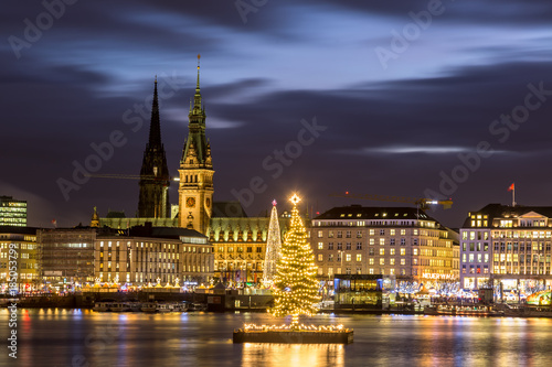 Christmas in Hamburg. Panoramic view of the decorated city center from Alster Lake, view to Hamburg Rathaus and a christmas tree installed in the center of the lake. Atmosphere before the New Year. 