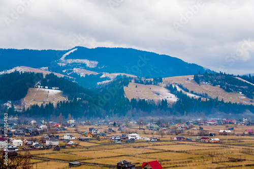 A winter panoramic landscape of the mountains and village in cloudy weather with the forest and snow on the top