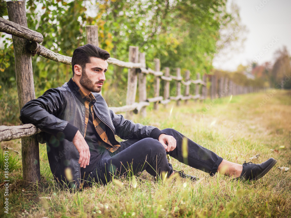 Portrait of sexy young man looking to a side while leaning on wooden fence in countryside Portrait of sexy young man looking to a side while leaning on wooden fence in countryside