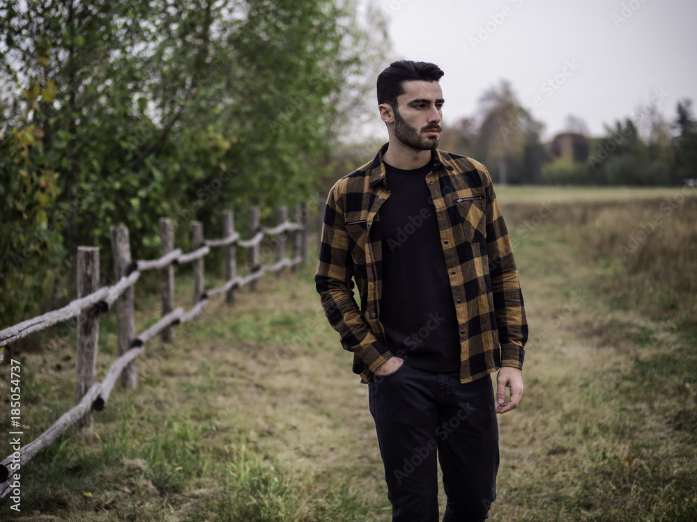 Portrait of sexy young man looking to a side near wooden fence in countryside next to a field or grassland Portrait of sexy young man looking to a side near wooden fence in countryside next to a field or grassland