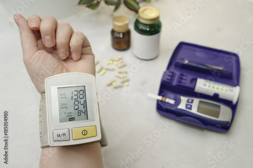 On the arm is a medical device that measures blood pressure. On the table is a glucometer and tablets.