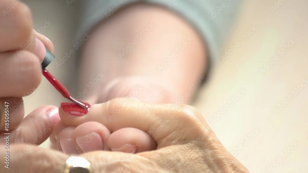 Manicurist applying red varnish to senior woman. Nail beautician painting nails to old woman in beauty salon close up.