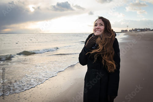 Young happy pretty woman in elegant clothes on the winter beach in NYC dreaming and smiling. One person. Winter season. Brighton Beach