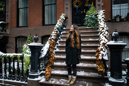 Young woman on a frosty winter Christmas morning standing on the porch of her house in New York city and smiling. One person