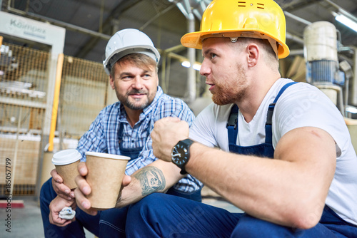 Portrait of two builders wearing hardhats taking break from work drinking coffee and resting on site