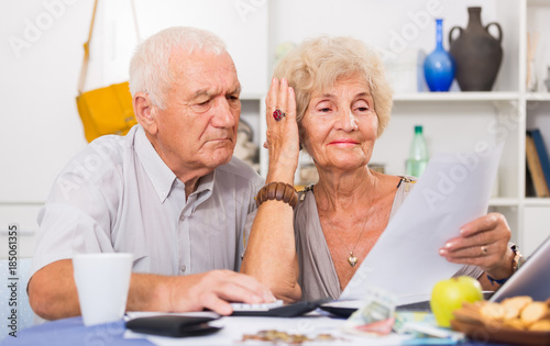 Worried mature man and woman analyzing bills