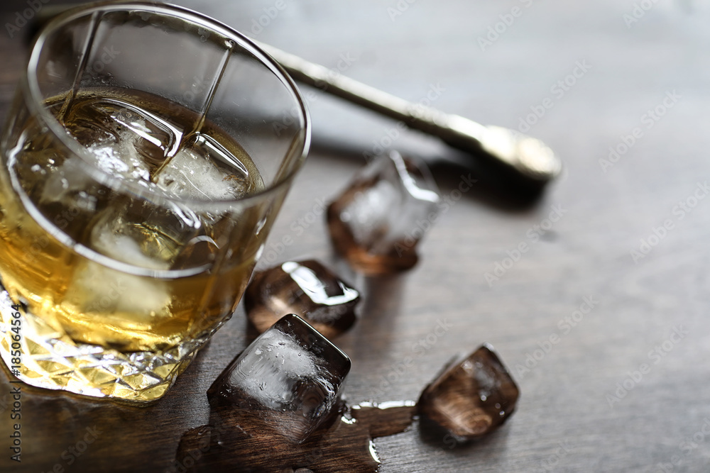 Whiskey in a glass and pieces of ice on a wood Whiskey in a glass and pieces of ice on a wood