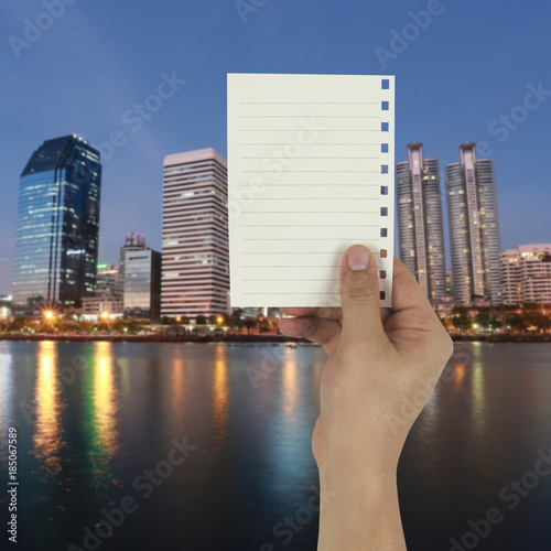 Hand of the businessman holding a empty paper note on twilight city background.
