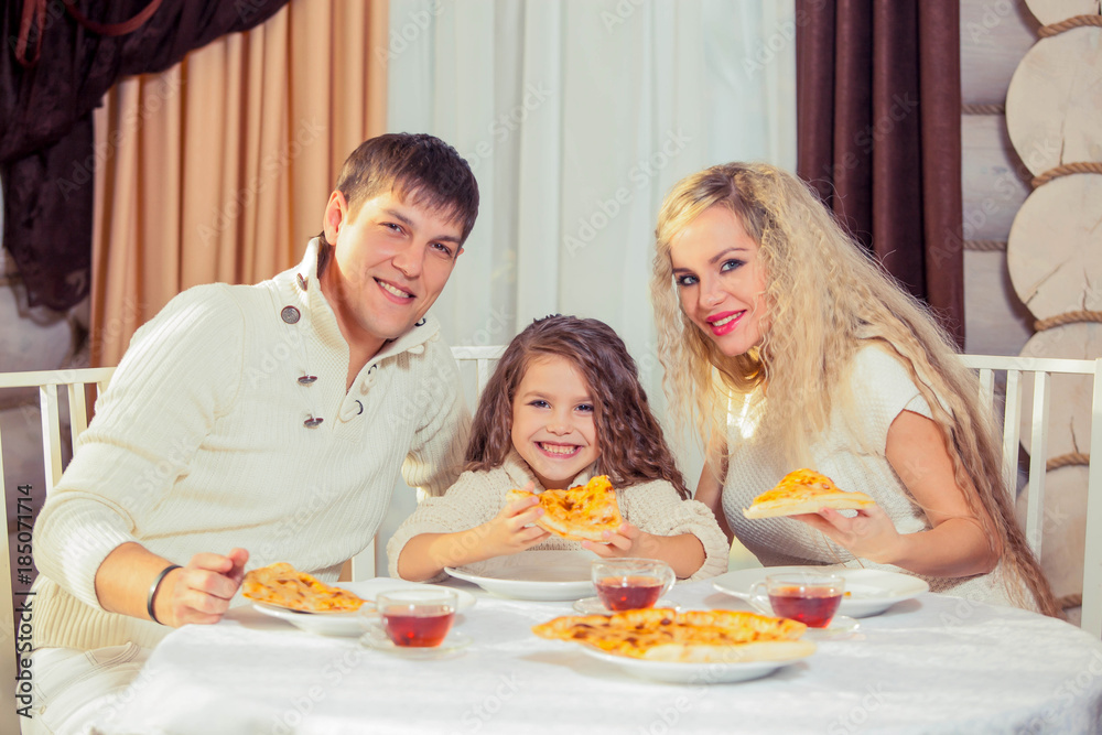 Family eating dinner at a dining table, Round table, pizza, orange, house made of wood Family eating dinner at a dining table, Round table, pizza, orange, house made of wood
