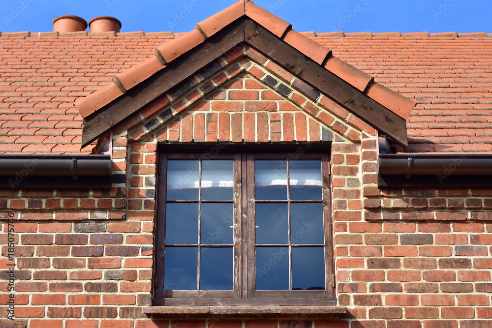 Dormer window with dark wooden frame on red brick cottage.