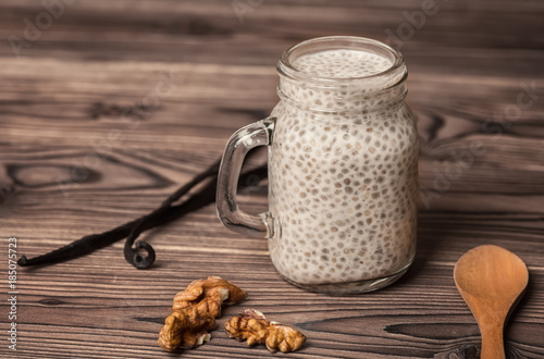 chia seed pudding in glass cup, walnuts, vanilla pods and spoon on wooden background, vegetarian food concept