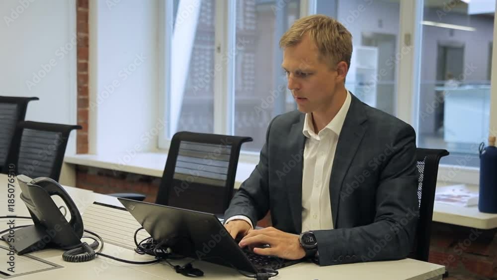 Male head is working at desk with laptop sitting in modern office. Attractive man looks attentively at screen of black pc, touches touchpad with fingers and types text of plan for upcoming meeting Male head is working at desk with laptop sitting in modern office. Attractive man looks attentively at screen of black pc, touches touchpad with fingers and types text of plan for upcoming meeting