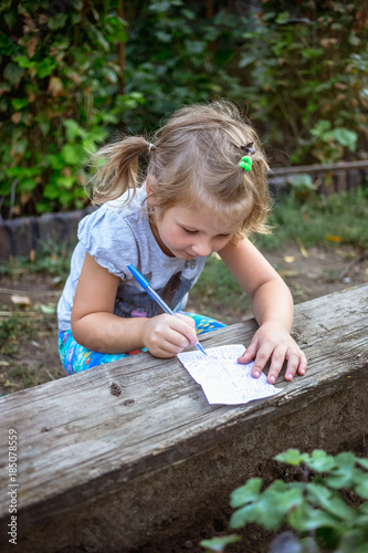 Cute little girl is drawing on paper in the garden.