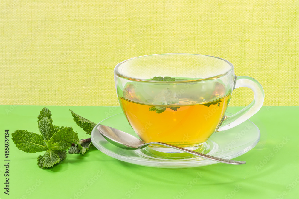 Tea with mint in glass cup on a green background