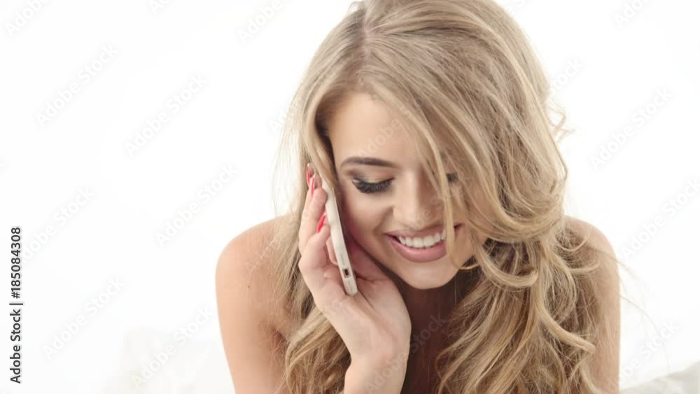 Smiling sexy woman looking at mobile phone lying down on the bed Smiling sexy woman looking at mobile phone lying down on the bed