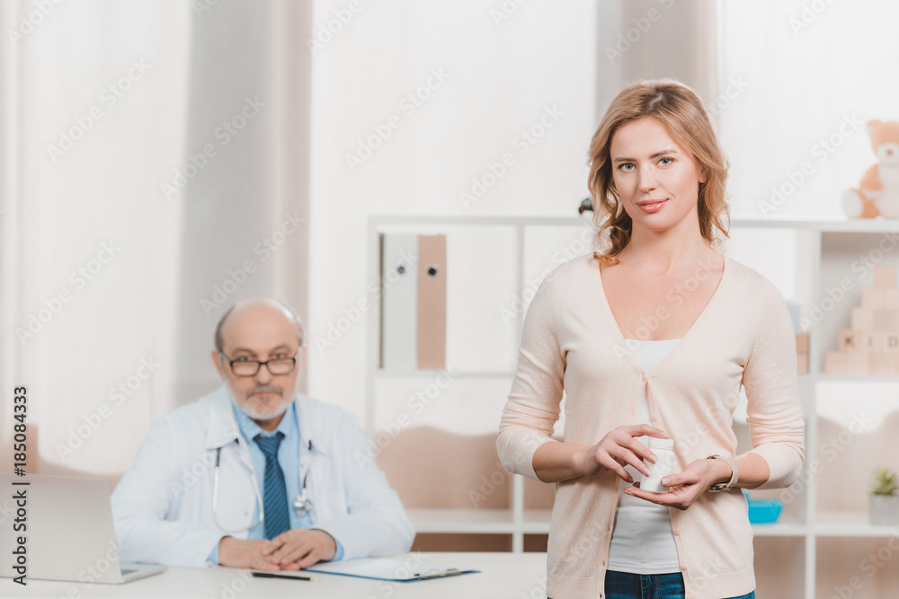 selective focus of woman with medicines in hands with senior doctor sitting at workplace in clinic selective focus of woman with medicines in hands with senior doctor sitting at workplace in clinic