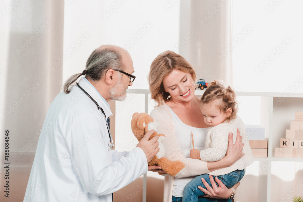 Obraz premium portrait of senior doctor, smiling mother with little girl on hands in clinic