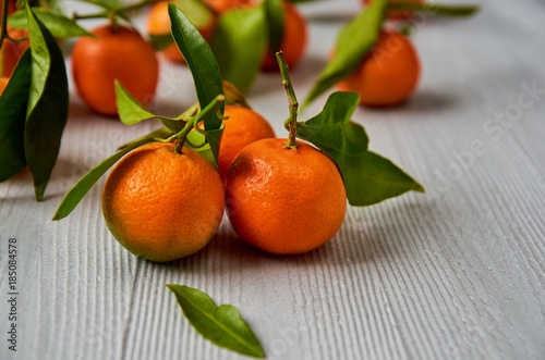 Three fresh tangerines with green leaves on the gray wooden board free copy space. Juicy orange mandarins and tangerine yellow on the blurred background. Citrus background. Close up view