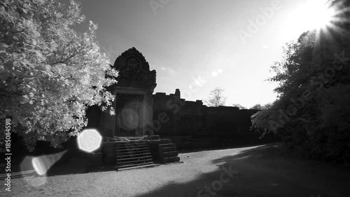 Moving out of the trees to reveal Banteay Srei temple ruins outer wall and getting lens flare from the sun. photo