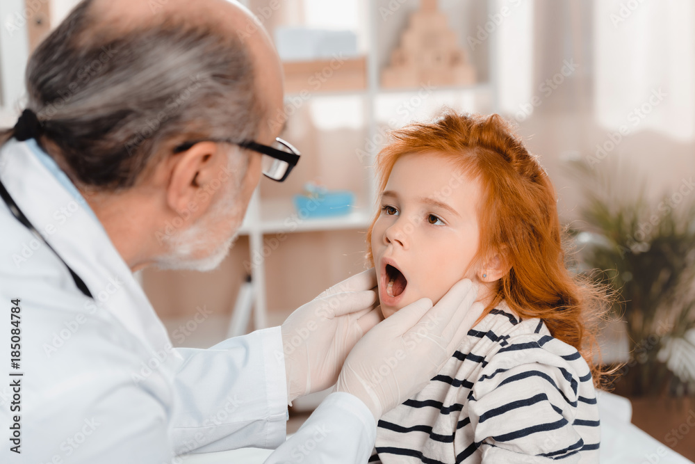 senior pediatrician in medical gloves examining little patients throat in clinic senior pediatrician in medical gloves examining little patients throat in clinic