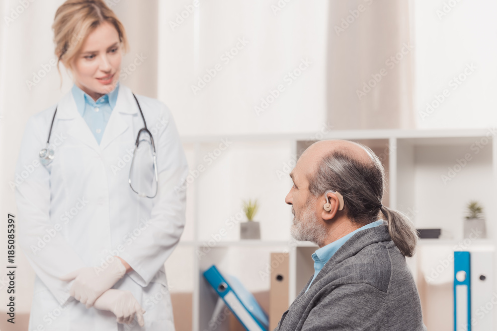 Fototapeta premium selective focus of senior patient with deaf-aid at doctors reception in clinic