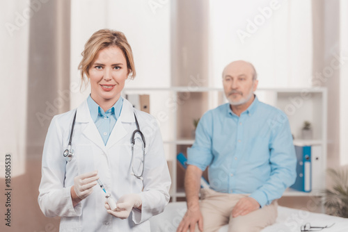 selective focus of doctor holding syringe for injection with senior patient behind in clinic