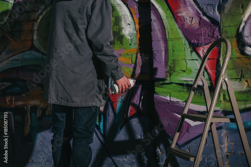 cropped view of street artist painting graffiti with aerosol paint on wall at night