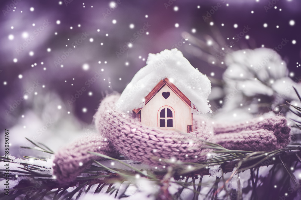 Christmas Toy house is wrapped in a warm scarf, it's snowing.on a natural natural background of a real fir in the snow, toned. Concept of winter, Christmas, new year,