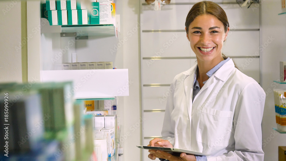 Portrait of a beautiful young girl (woman) pharmacist, consultant, working at a pharmacy, selling and checking medication, smiling, giving advice. Concept: profession, medecine, medical education.