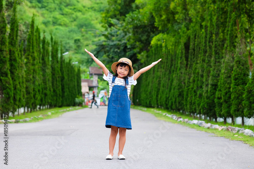 Asian child girl smiling with her arms raised on both sides of the road. With green trees