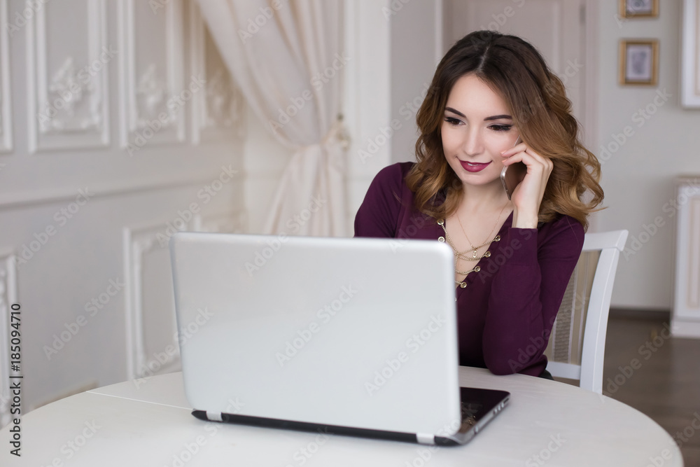 A beautiful woman is sitting behind a laptop in the kitchen, a realtor. Talk on the phone, smartphone. A beautiful woman is sitting behind a laptop in the kitchen, a realtor. Talk on the phone, smartphone.