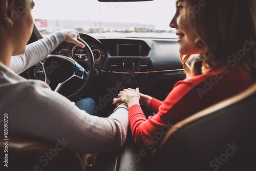 Family young couple sitting in the car holding hands sitting in the car, the man driving with his hand on the steering wheel