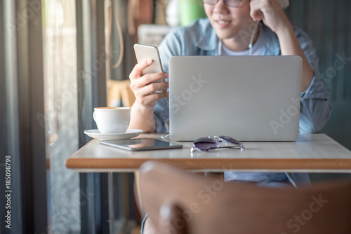 Young Asian entrepreneur man using smartphone and laptop computer in cafe, freelance lifestyle or digital nomad concepts