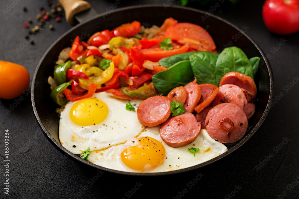 Breakfast. Fried eggs with sausage and vegetables in a frying pan on a black background in rustic style. Breakfast. Fried eggs with sausage and vegetables in a frying pan on a black background in rustic style.