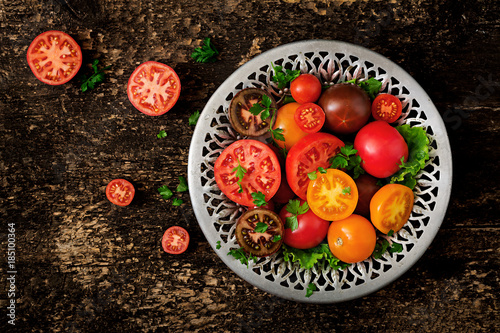 Tomatoes of different colors with green herbs in a bowl on a black background. Flat lay. Top view