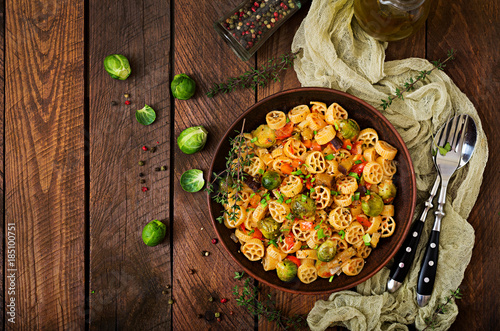 Vegetarian Vegetable pasta Rocchetti with brussels sprouts, tomato, eggplant and paprika in brown bowl on wooden table. Top view