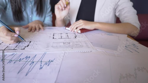 Two female realtors prepares for the presentation sitting in the office. The papers with the house schemes and market prices charts lie on the big wooden table and professional outlines the important