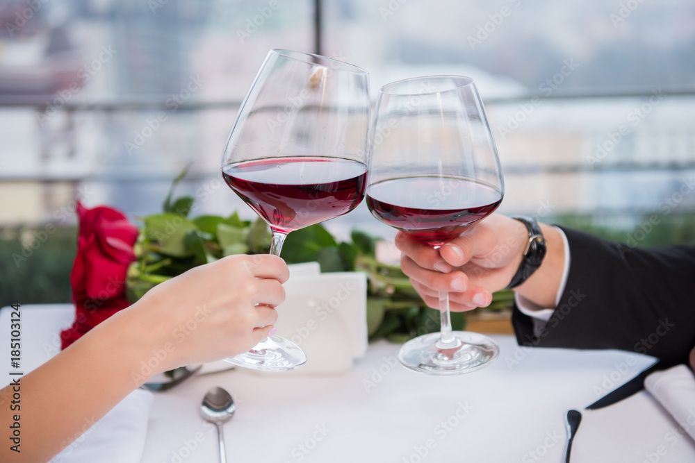 cropped shot of couple clinking glasses of red wine while celebrating st valentine day in restaurant