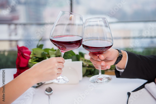 cropped shot of couple clinking glasses of red wine while celebrating st valentine day in restaurant