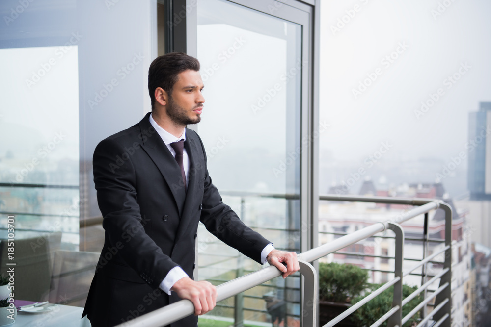 portrait of young pensive man in suit standing at balcony portrait of young pensive man in suit standing at balcony