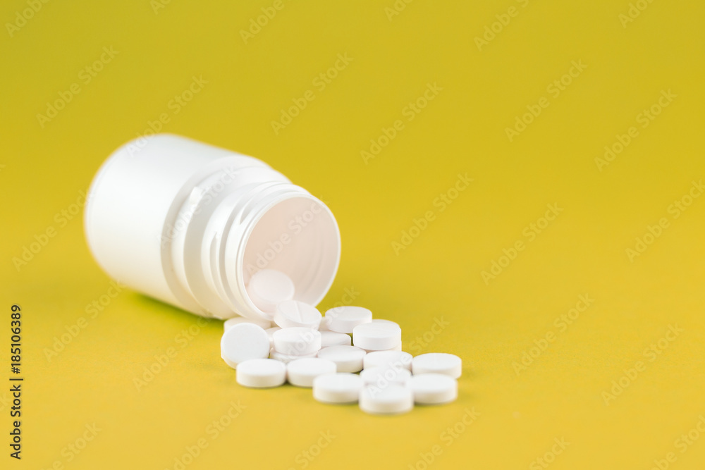 Close up white pill bottle with spilled out pills on yellow lime background with copy space. Focus on foreground, soft bokeh. Pharmacy drugstore concept Close up white pill bottle with spilled out pills on yellow lime background with copy space. Focus on foreground, soft bokeh. Pharmacy drugstore concept
