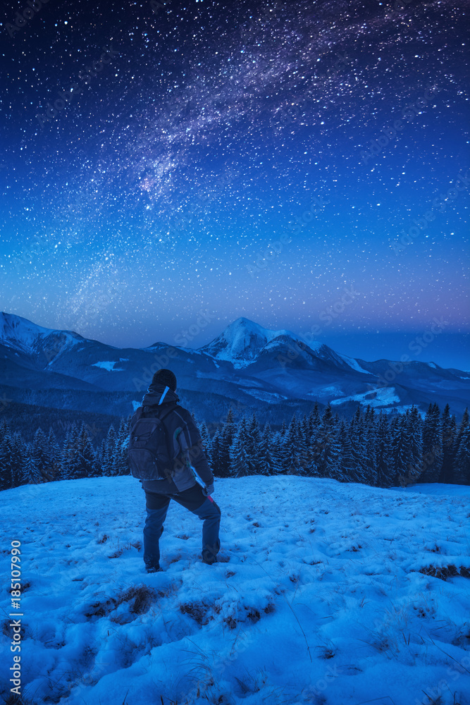 A hiker man with backpack standing on a snowy slope at night A hiker man with backpack standing on a snowy slope at night
