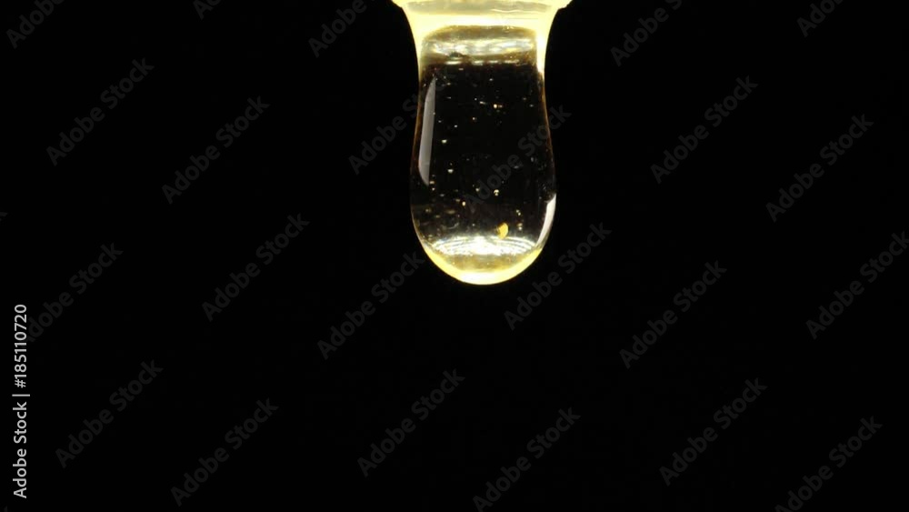 Thick honey drop dripping on black background. Macro shot. Thick honey drop dripping on black background. Macro shot.